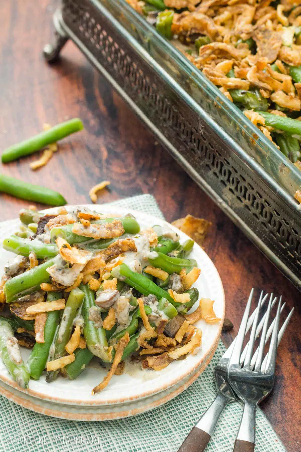 Fresh green bean casserole on a small white plate in front of a decorative casserole dish.