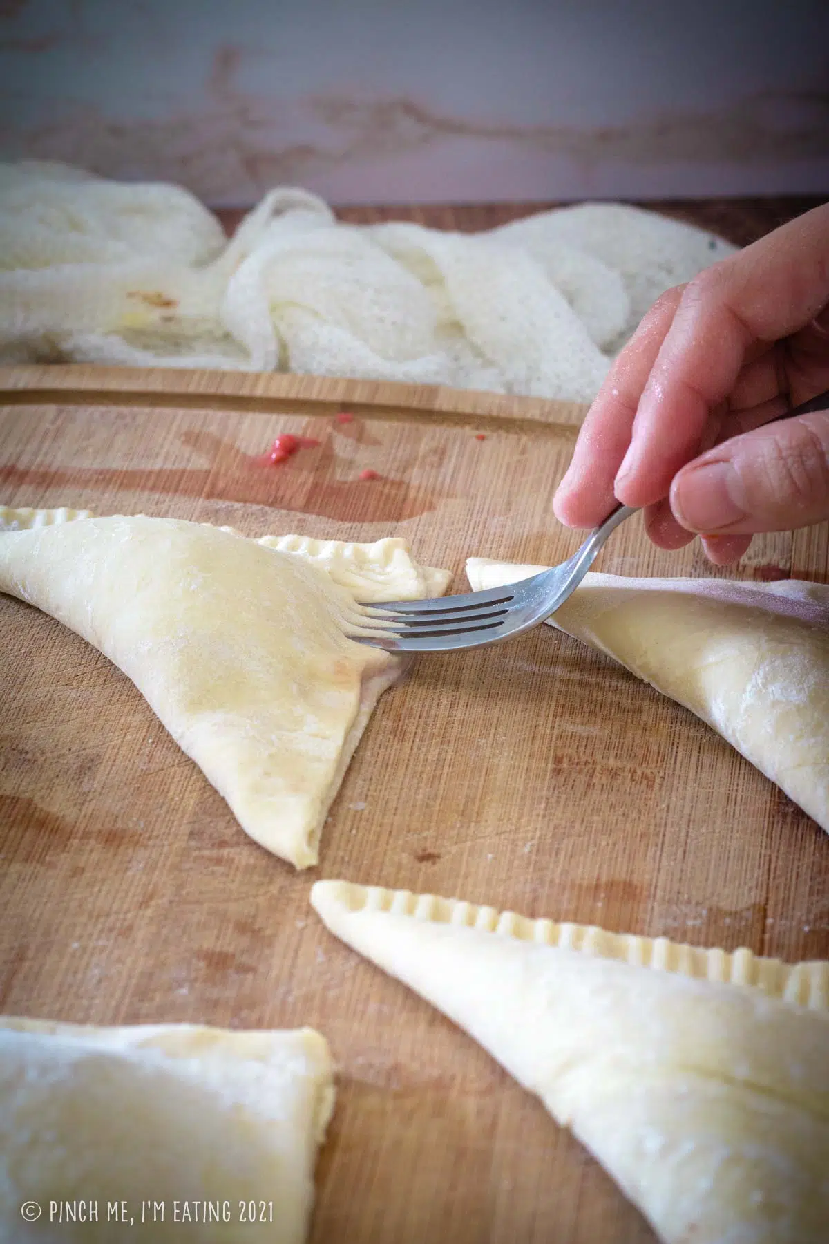 Puff pastry turnovers being crimped with a fork.
