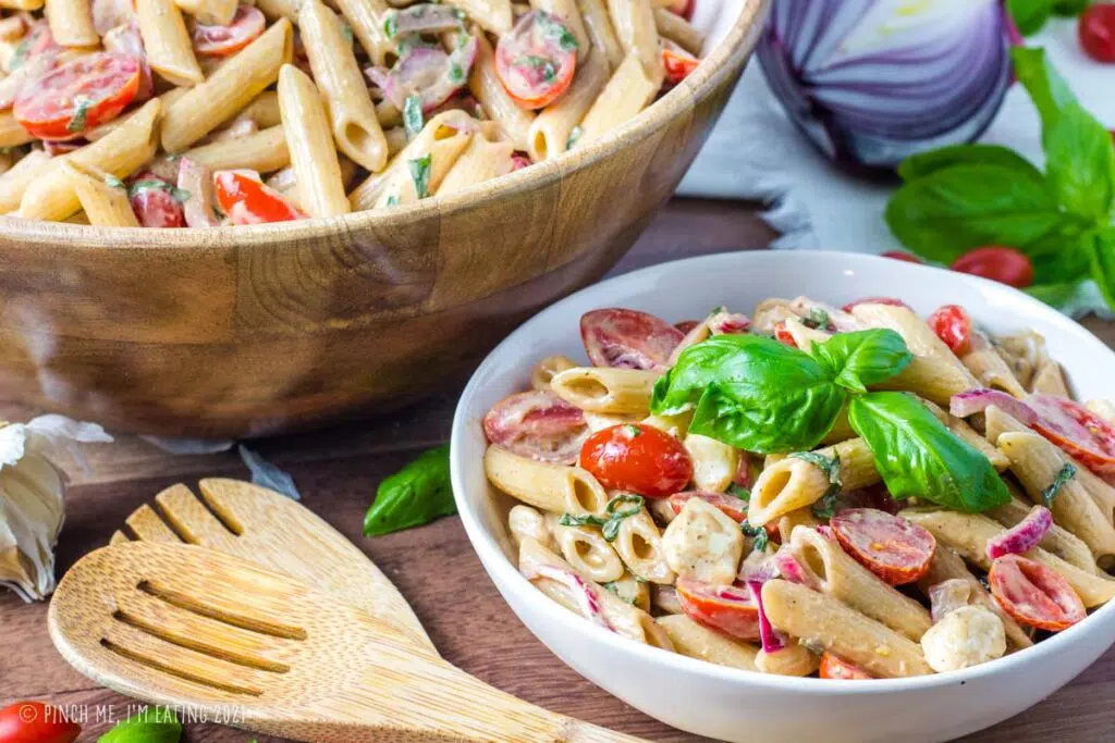 Caprese pasta salad in a white bowl in front of a wooden serving bowl.