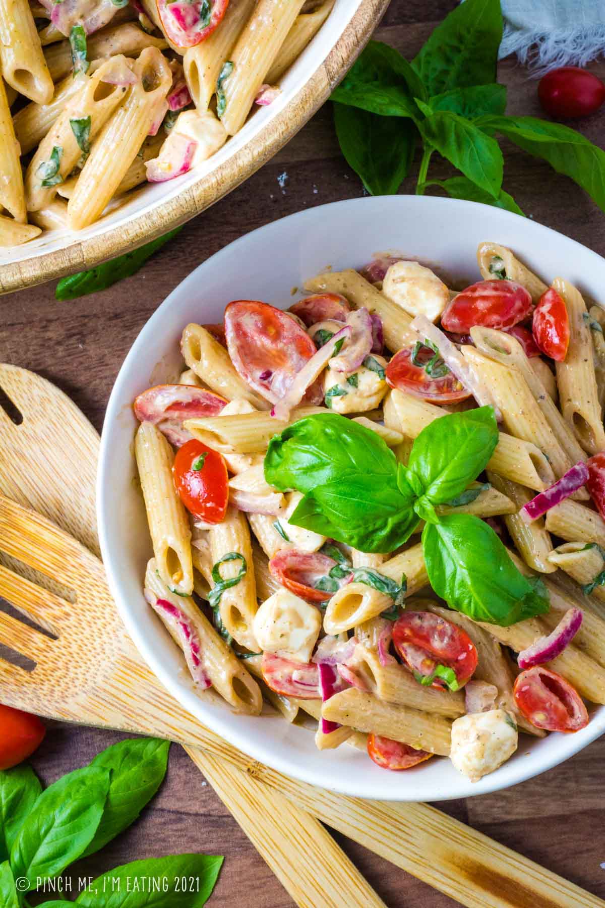 Overhead view of creamy balsamic caprese pasta salad in a white bowl.