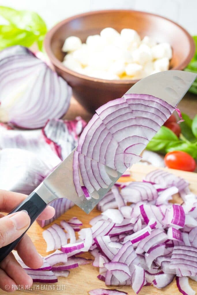 Red onion slivers on the side of a knife.