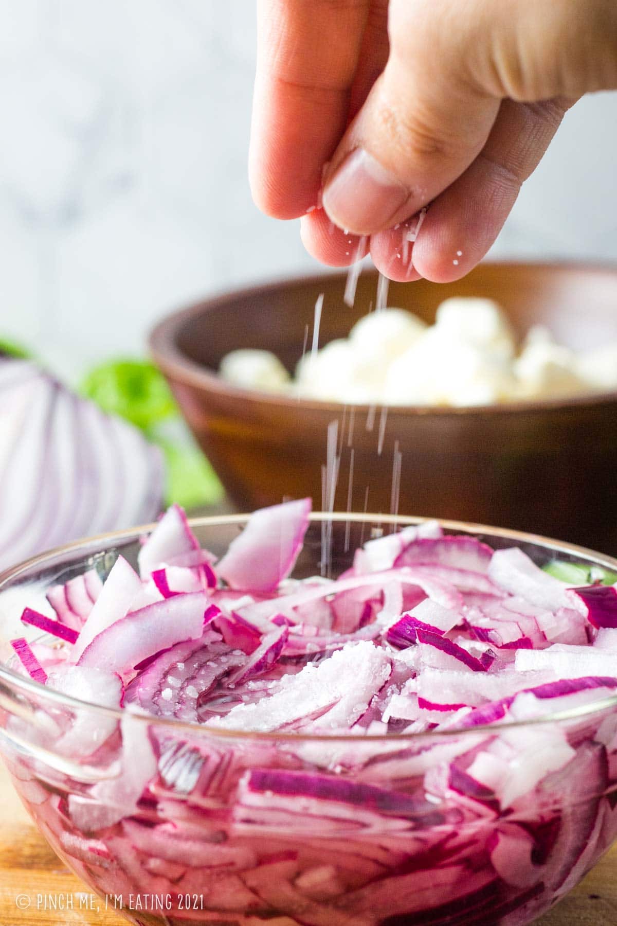 Sprinkling salt into bowl of red onion pieces and white vinegar.