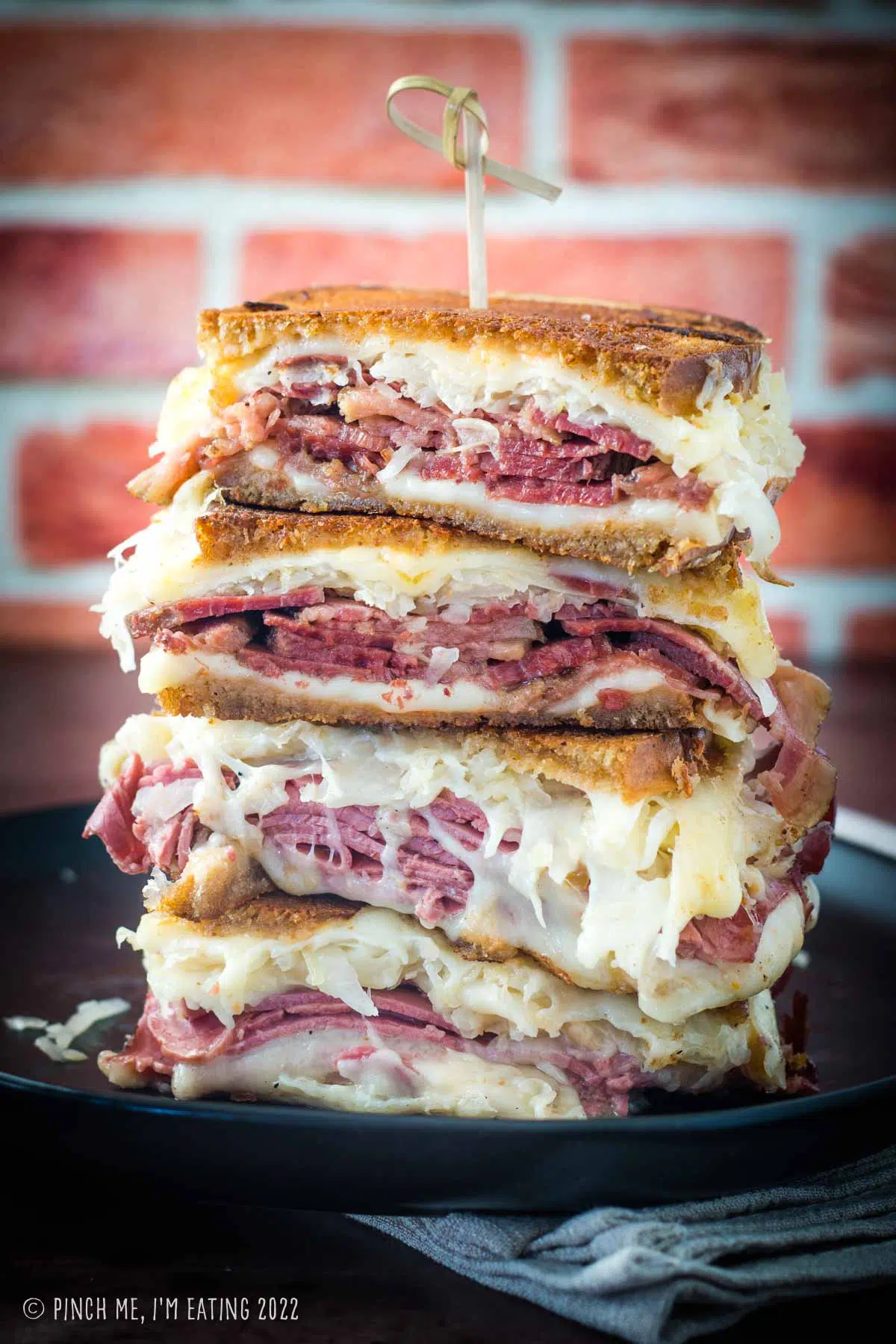 Four stacked corned beef reuben halves with melty cheese and toasted rye bread on a black plate.