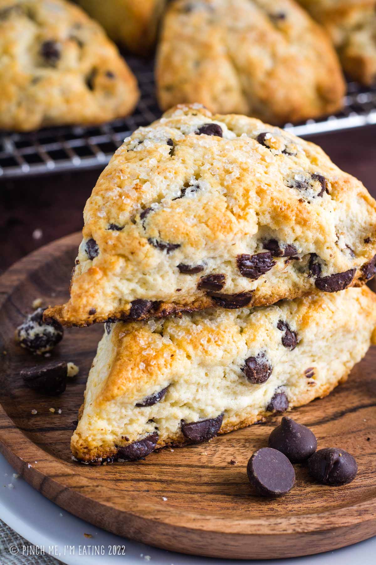 Two dark chocolate chip scones stacked on a wooden plate.