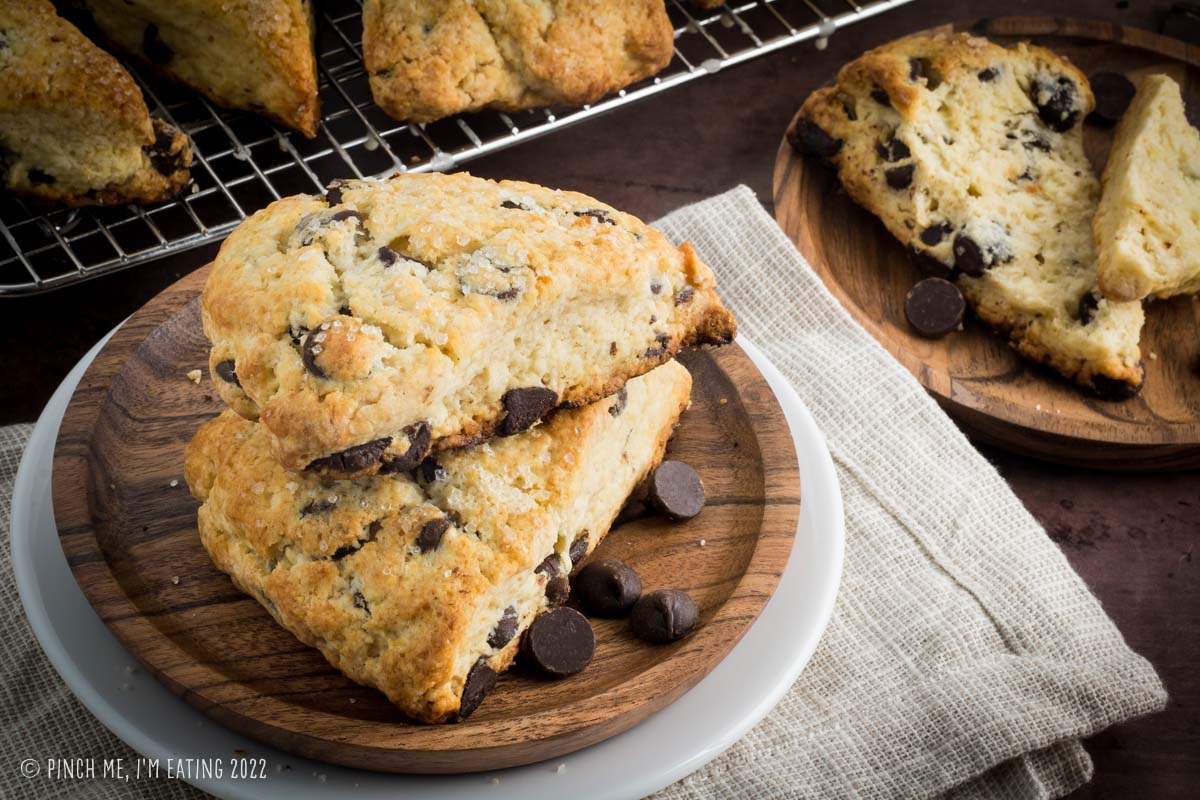 Two dark chocolate chip scones on a small wooden plate, with an open scone on another wooden plate in the background.