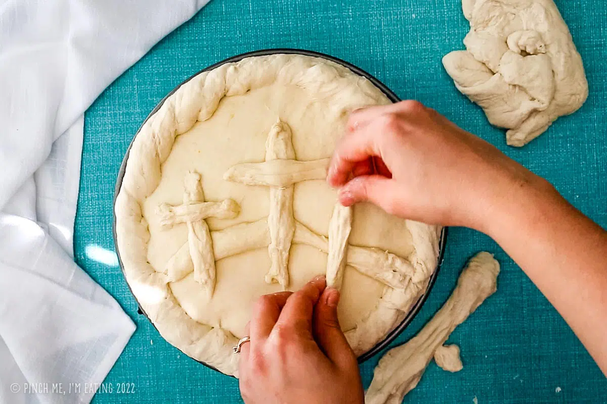 Hands decorating Pizza Rustica with three crosses made of pizza dough.