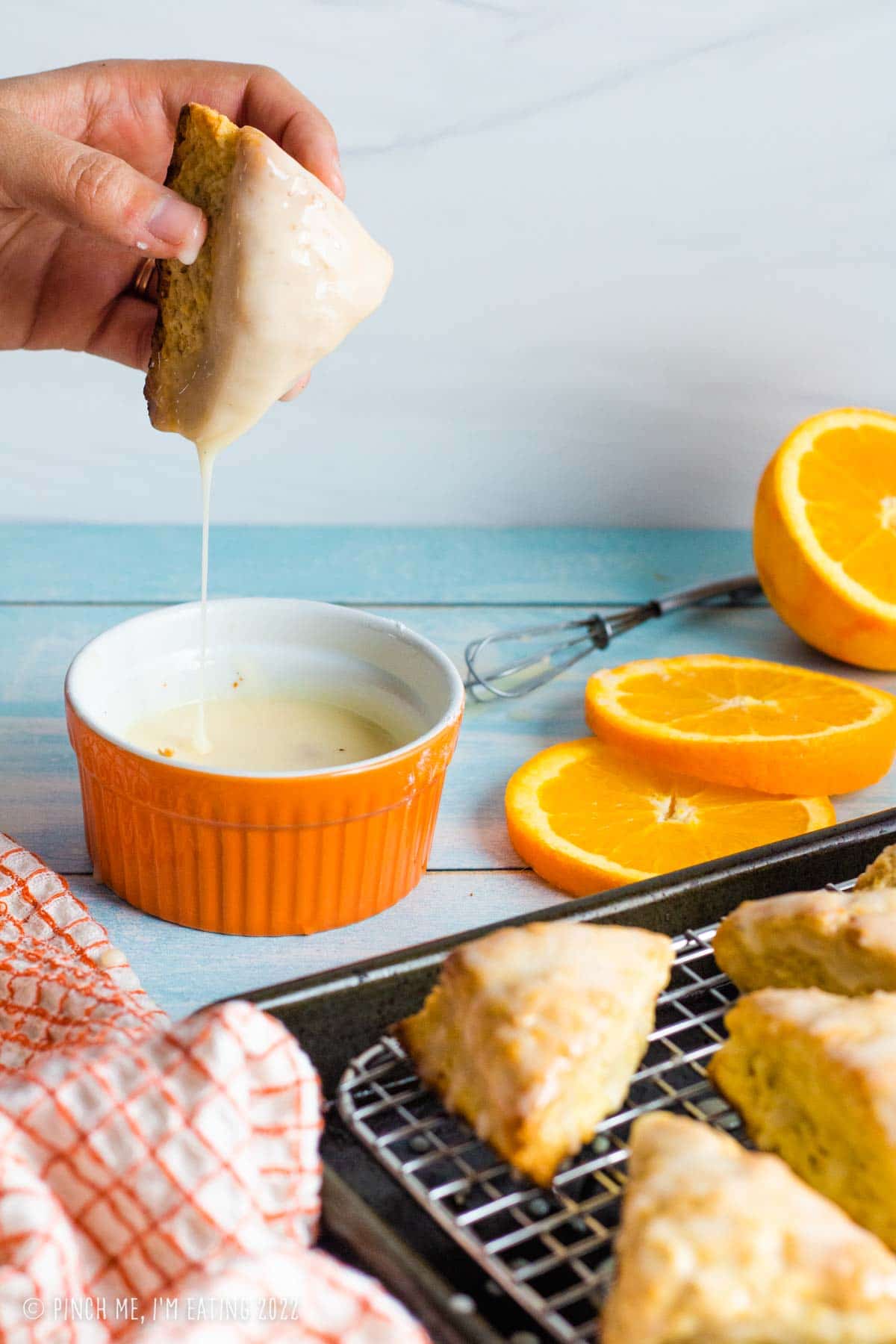 Hand holding freshly glazed homemade orange scone dripping into orange ramekin.