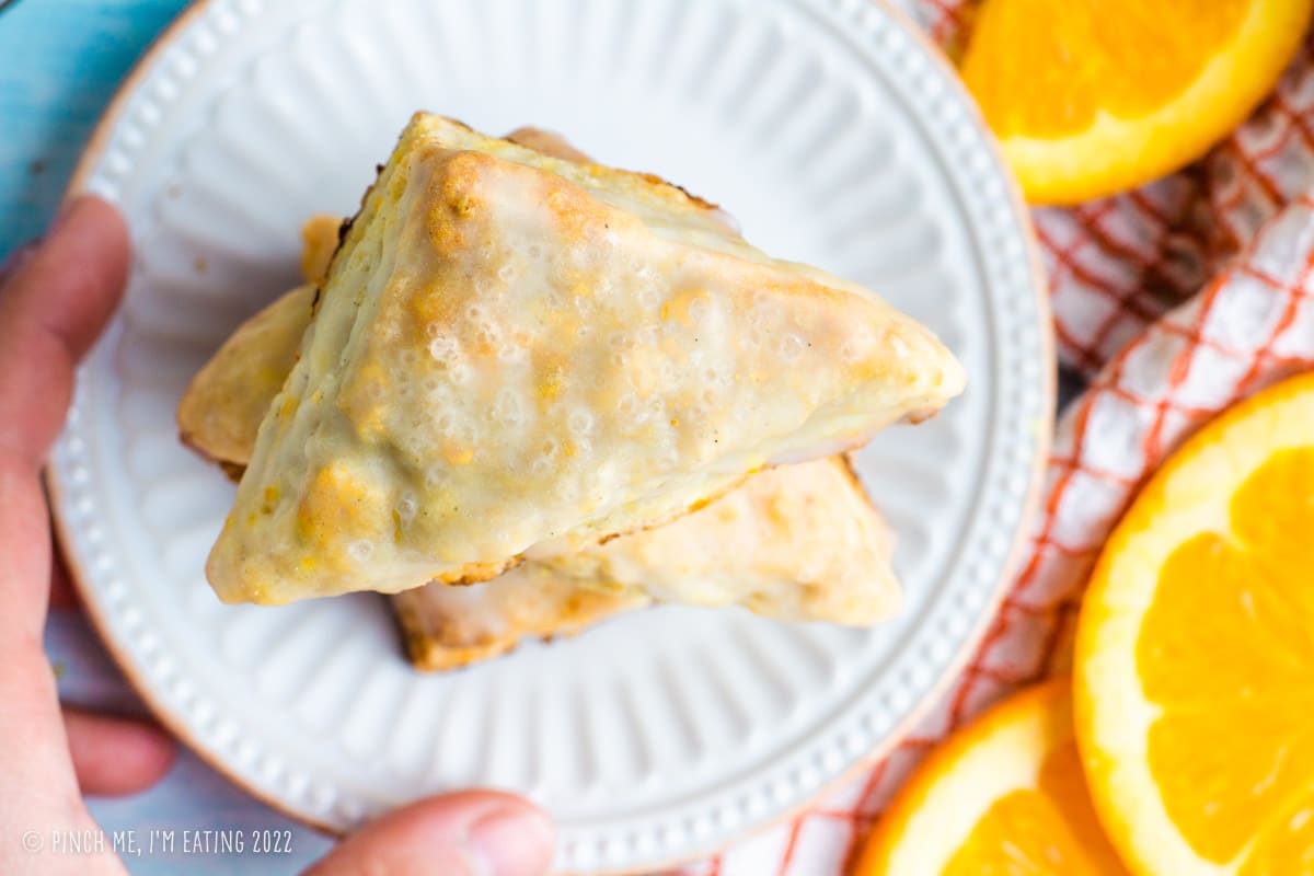Overhead shot of glazed orange scones with coarse sanding sugar on a white plate.