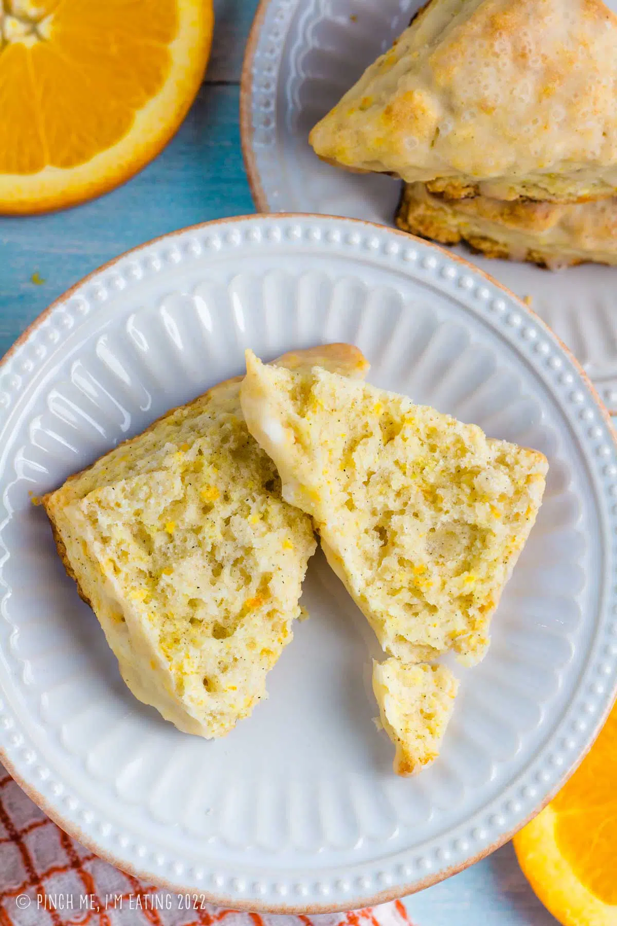 Overhead view of flaky orange scone with fresh orange zest split in half on a white plate.