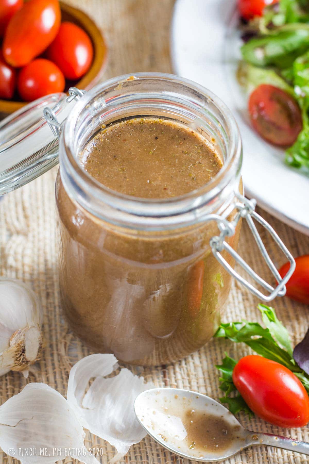 Creamy honey balsamic dressing in a jar with grape tomatoes and mixed greens in the background.