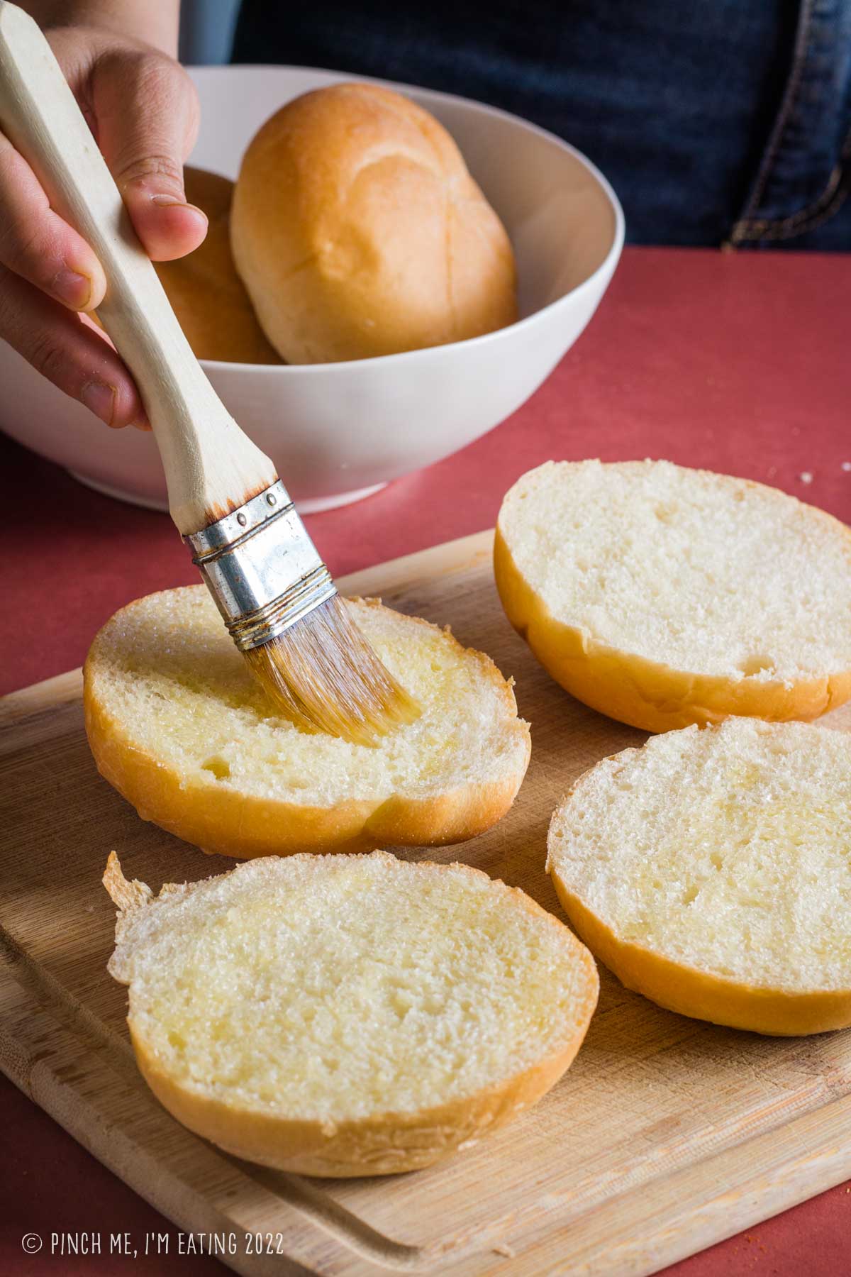 Brushing melted butter on split sandwich rolls.