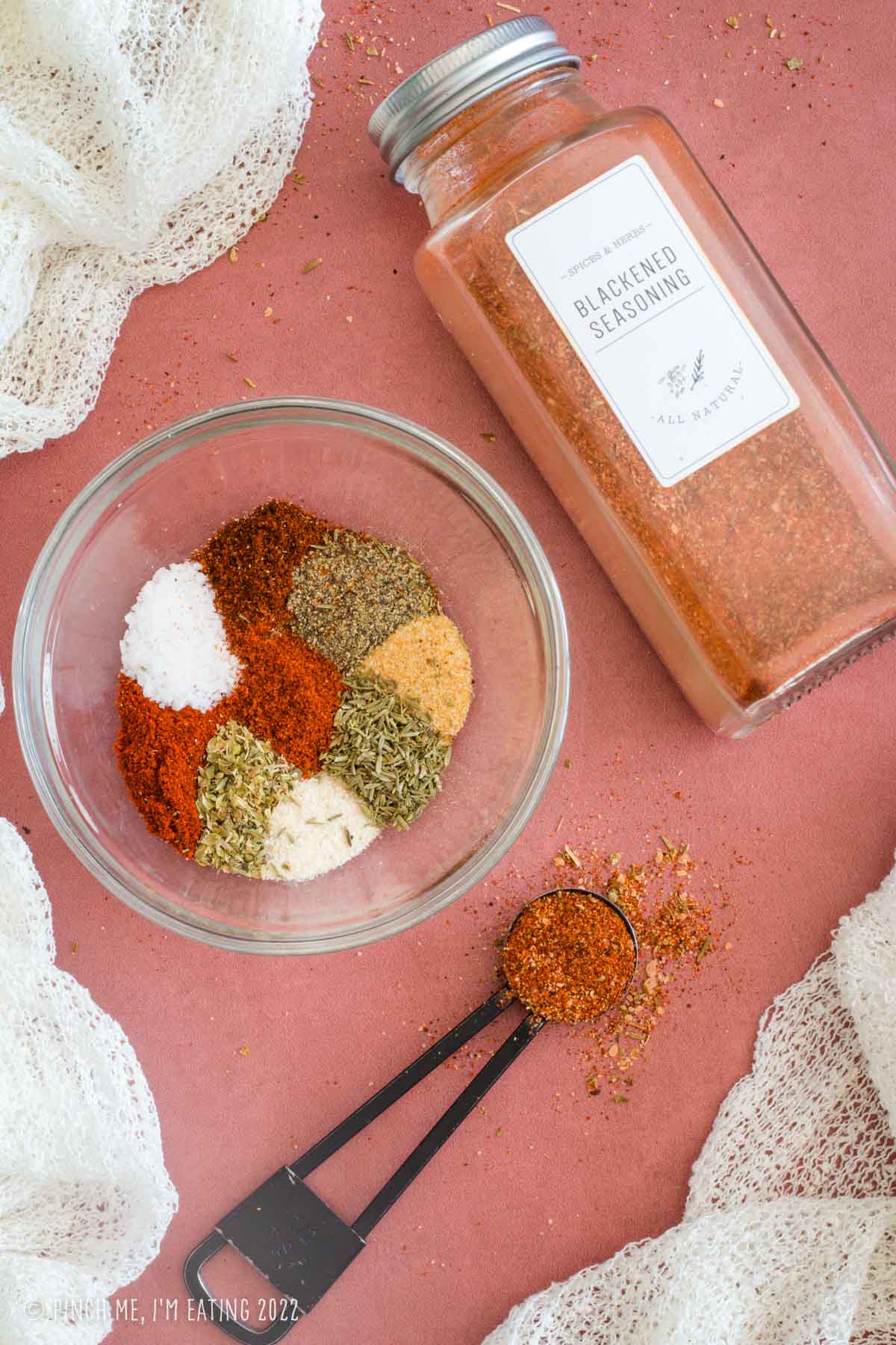 Ingredients for blackened seasoning in a glass bowl alongside a spice jar of already-mixed homemade blackened seasoning.