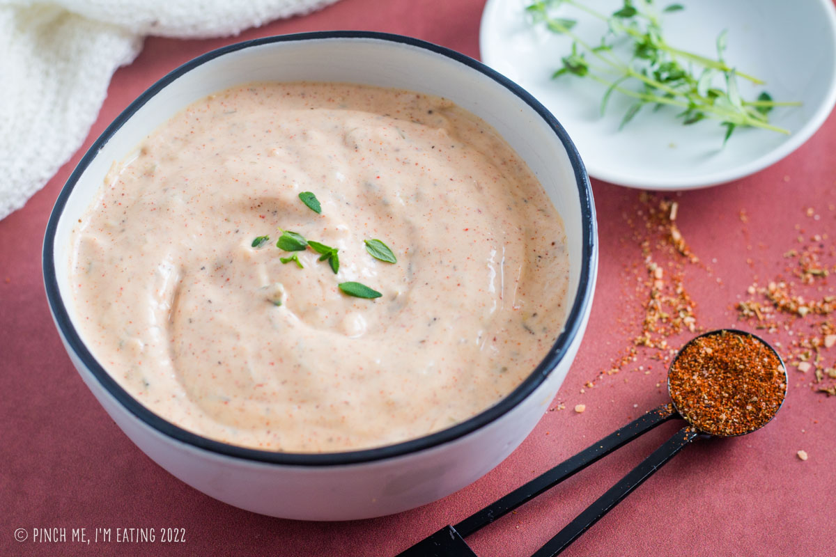 Easy homemade Cajun remoulade sauce in a white bowl garnished with fresh thyme next to a spoonful of blackened seasoning.