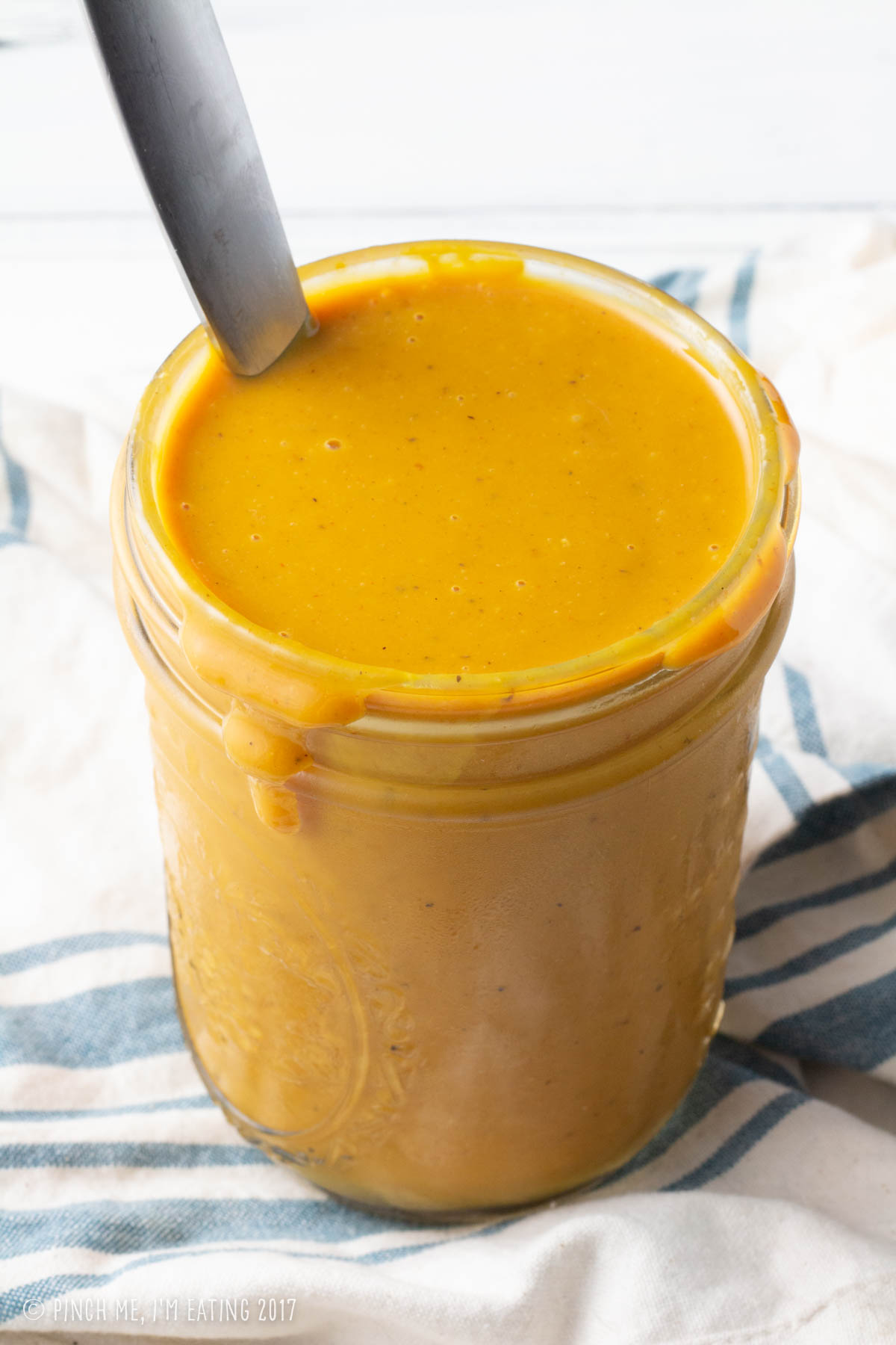 Golden yellow Carolina mustard bbq sauce in a mason jar with a spoon emerging.