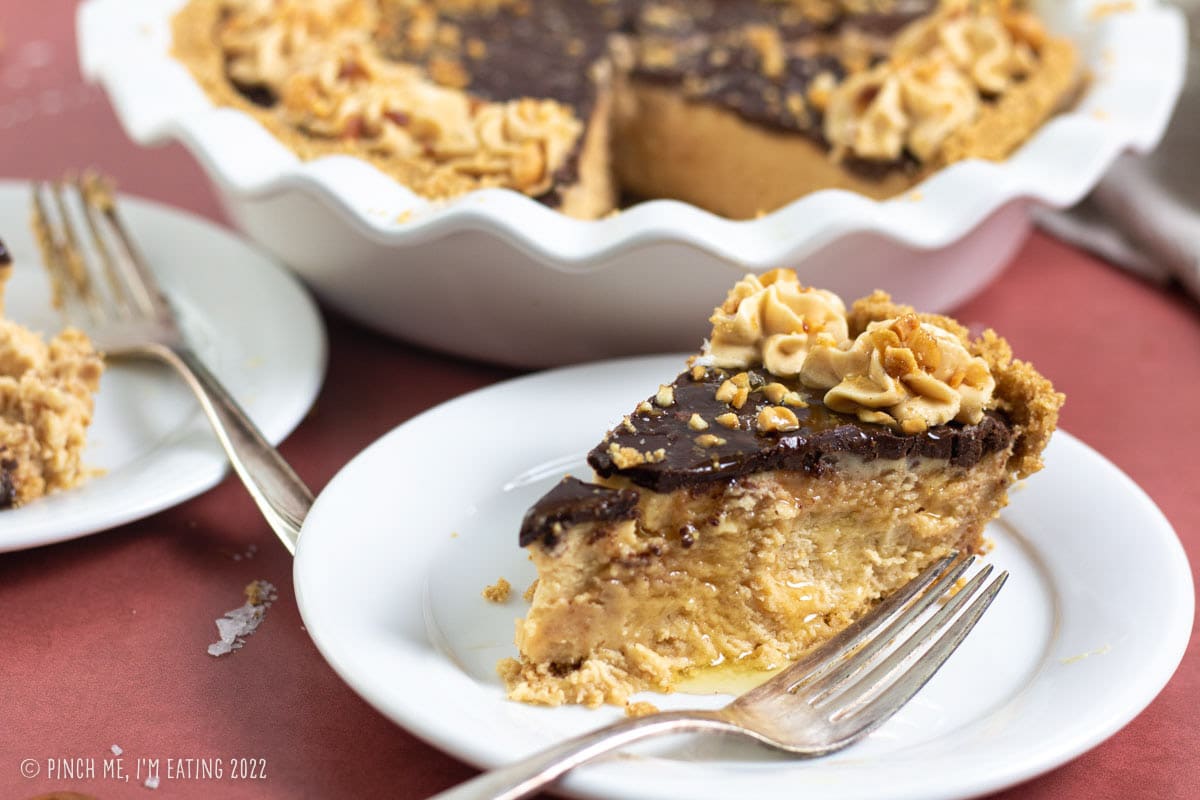 Slice of peanut butter mousse pie on a white plate with graham cracker crust and chocolate ganache.