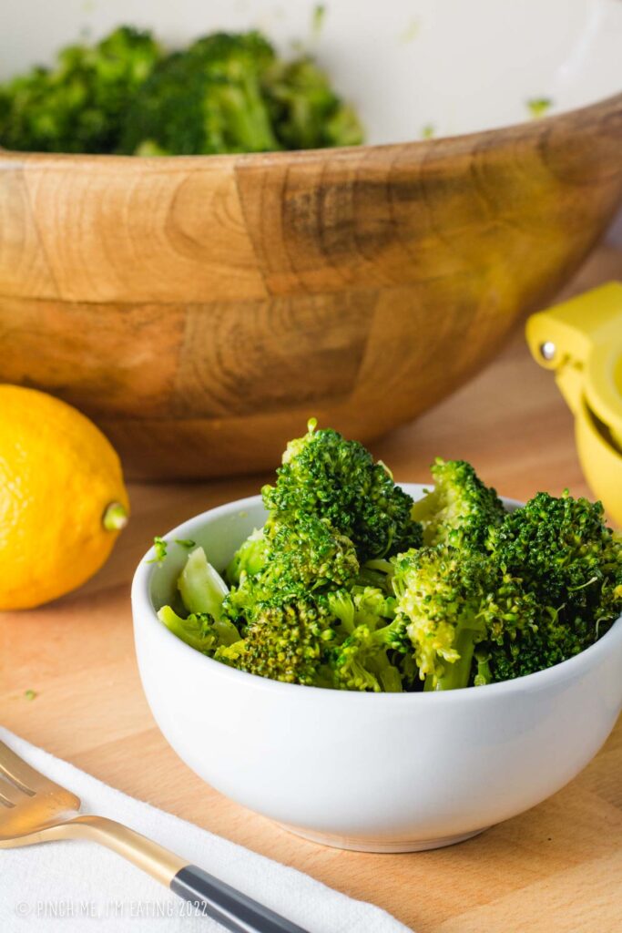 Lemon broccoli salad in a small white bowl in front of a large wooden serving bowl.