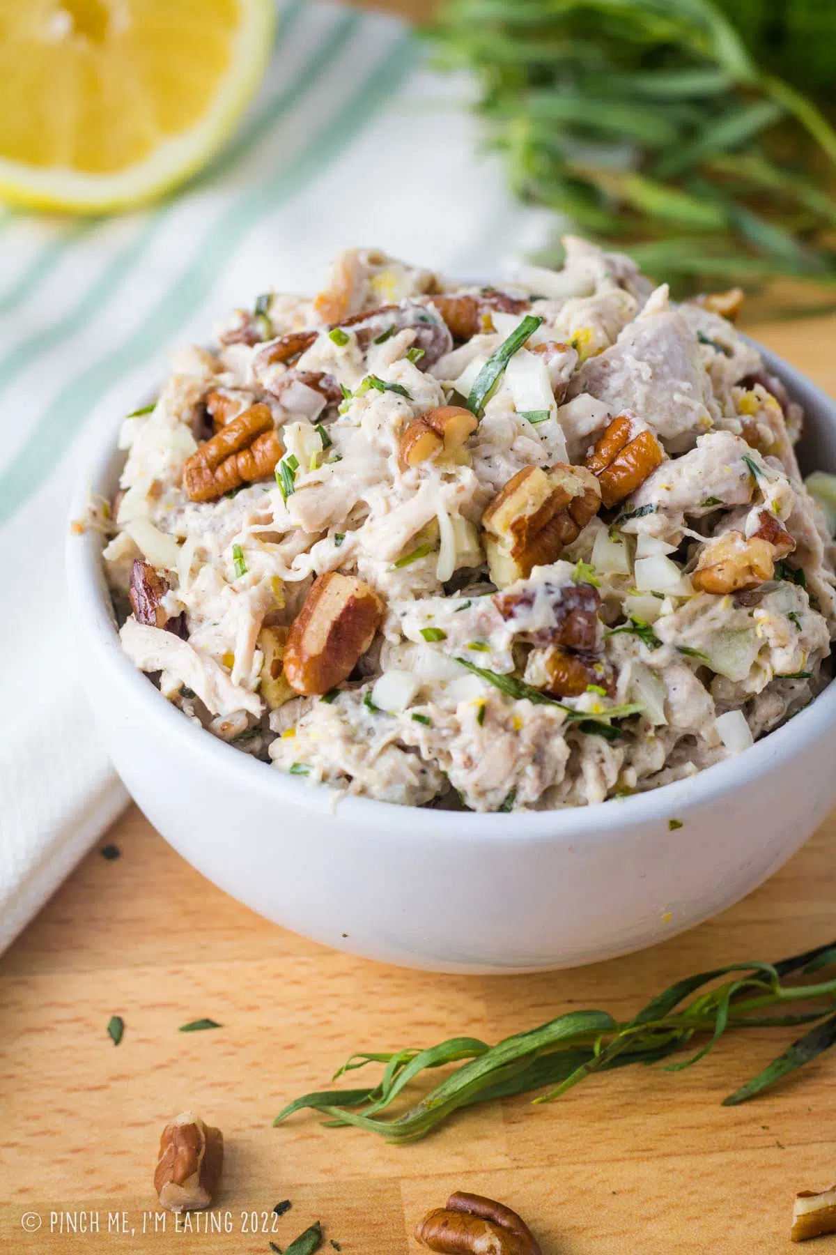 Lemon tarragon shredded chicken salad topped with pecans in a white bowl.