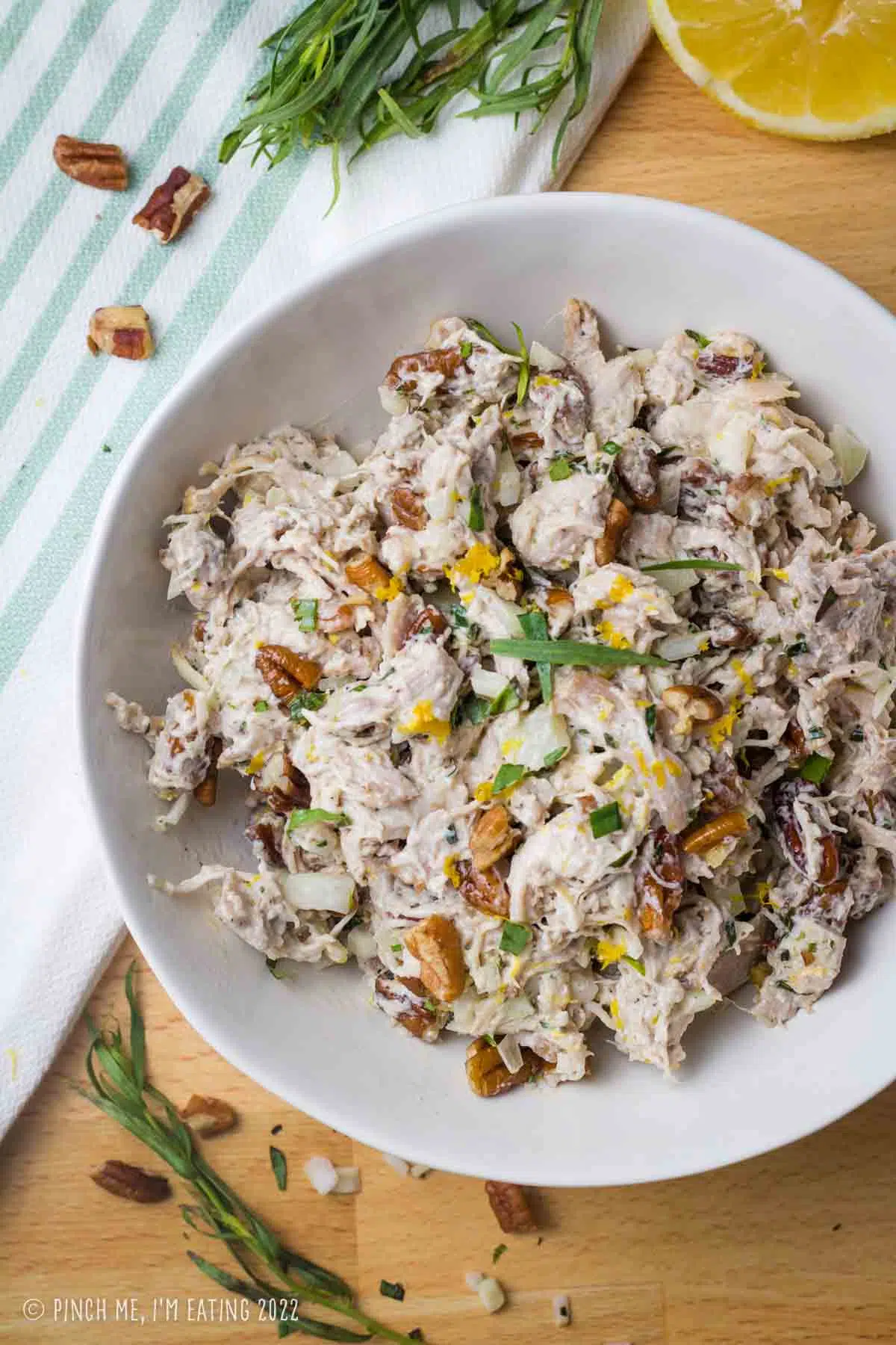Lemon tarragon shredded chicken salad topped with pecans and lemon zest in a white bowl.