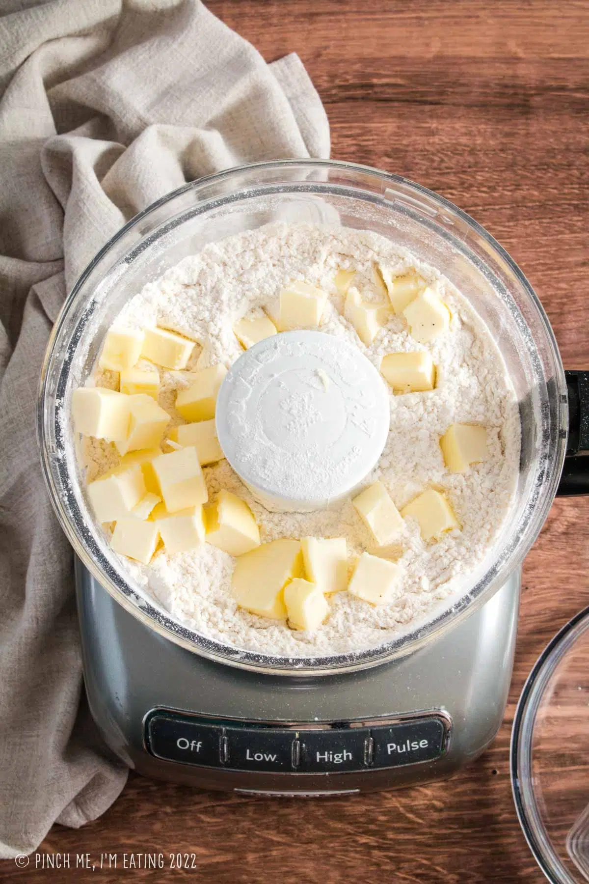 Overhead view of food processor with dry ingredients and cold butter cubes for making scones.
