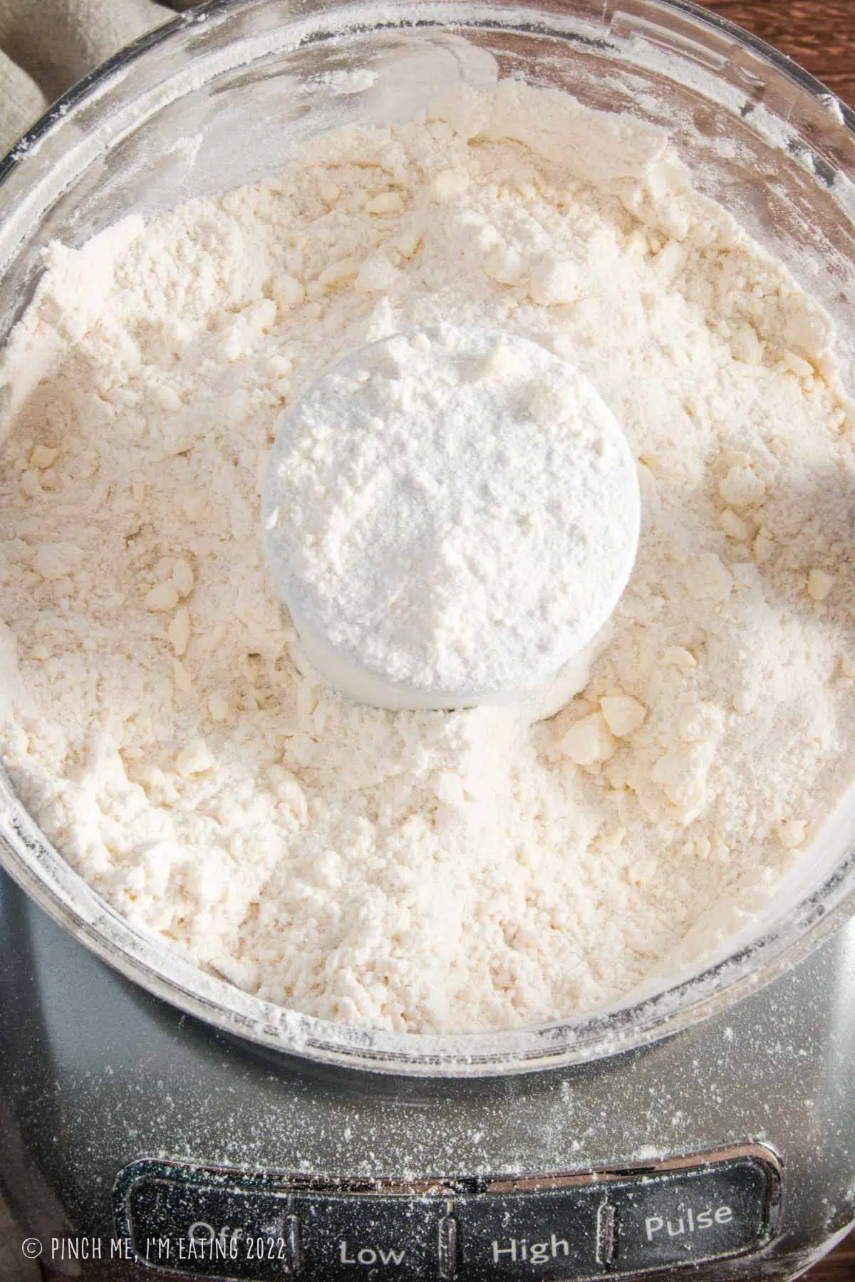 Overhead view of food processor showing texture of butter cut into dry ingredients for making scones.