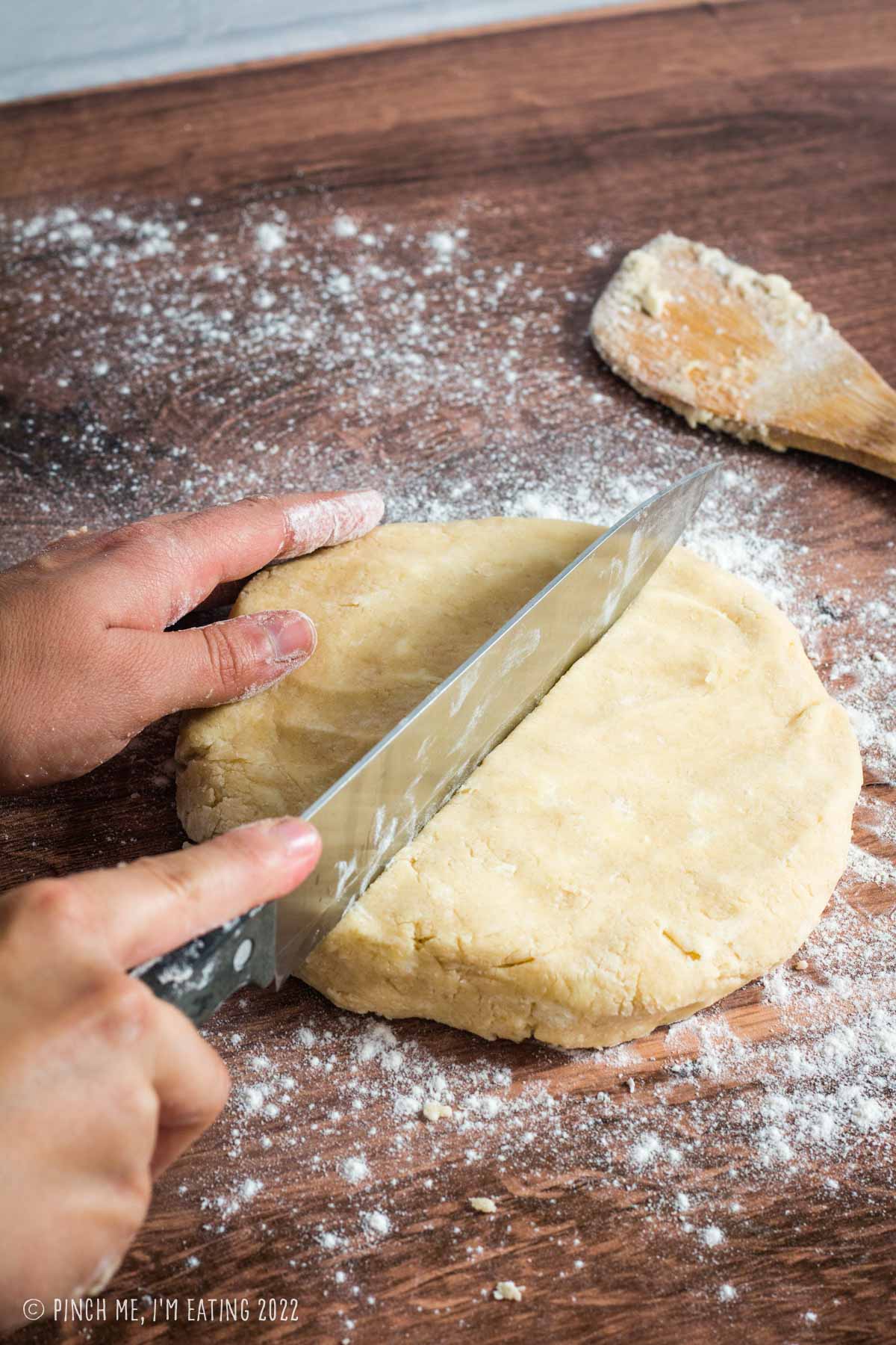 A circle of scone dough being cut in half with a large knife.