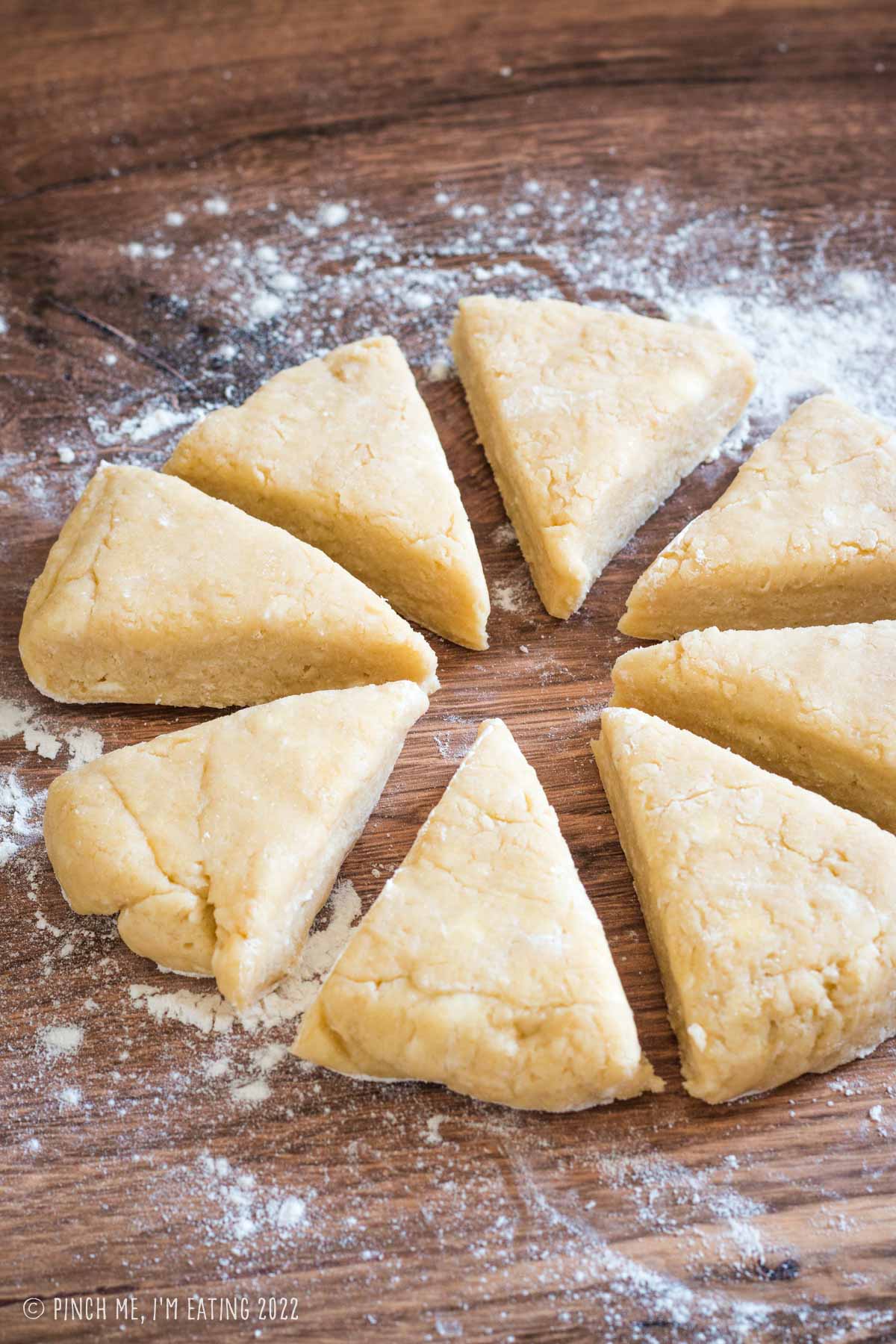 A round of plain scone dough cut into eight wedges on a flour-dusted wood surface.