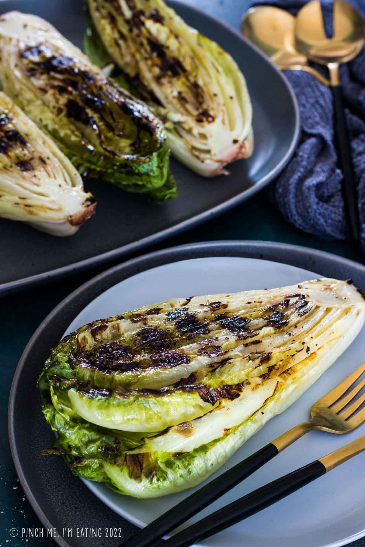 Grilled heart of romaine on a gray plate with gold fork.