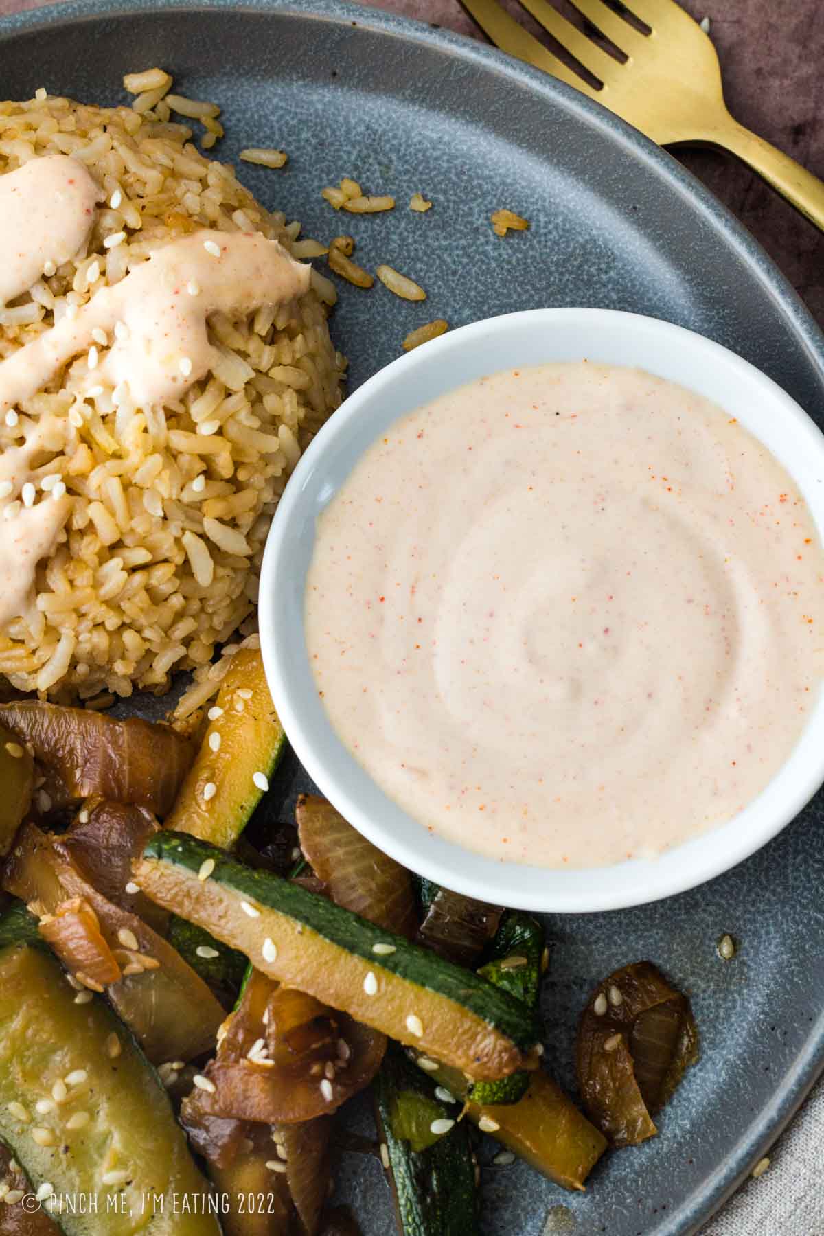 Yum yum sauce (Japanese white sauce) in a dipping sauce bowl on a plate with hibachi rice and zucchini.