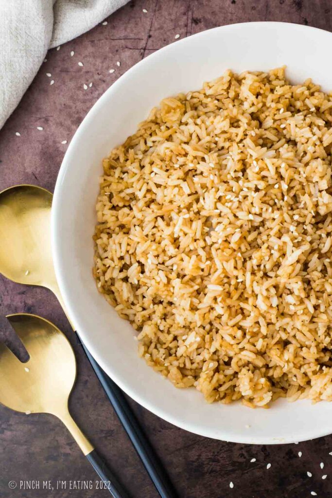 Sesame Hibachi fried rice in a white bowl with gold and black serving utensils.
