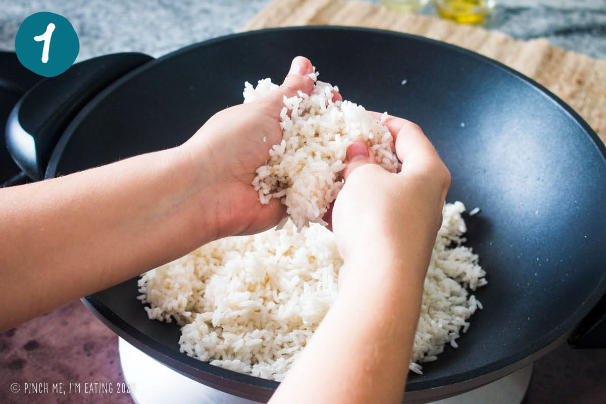 Hands crumbling cold leftover white rice into a wok.