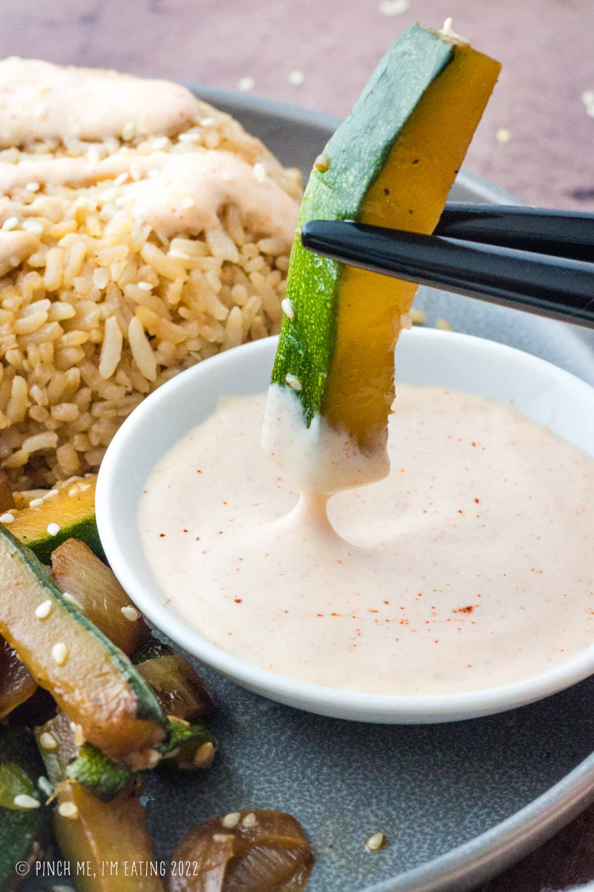 Chopsticks dipping zucchini stick into Yum Yum Sauce (Hibachi white sauce).