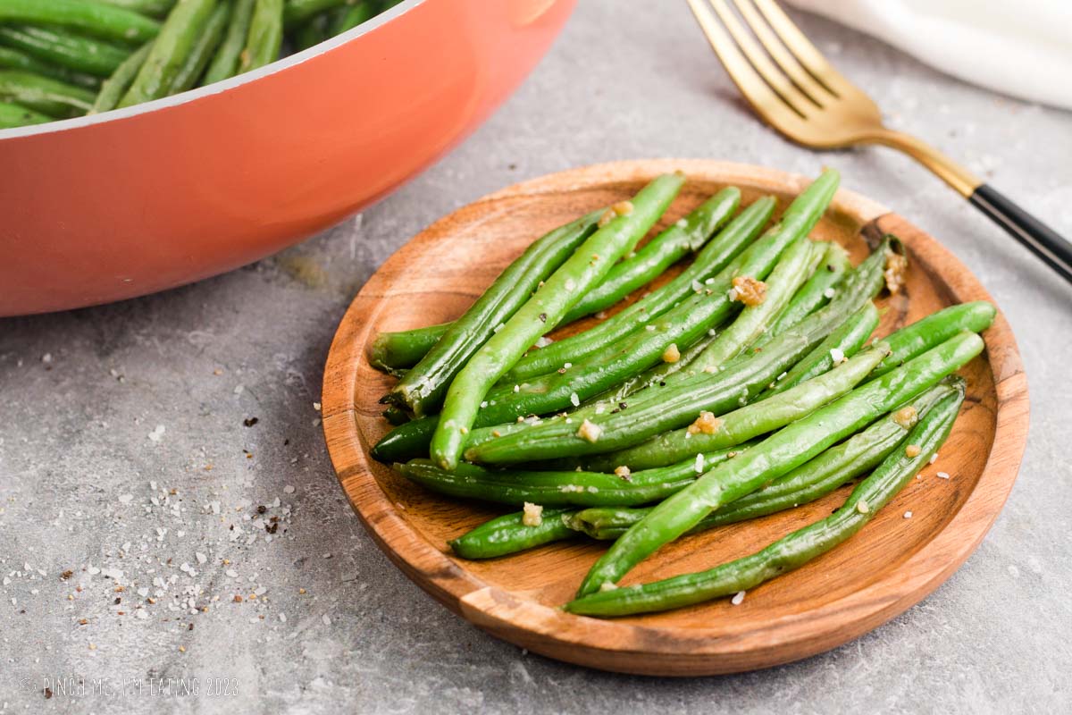 Steakhouse style buttery garlic green beans on a wooden plate.