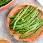 Steakhouse style garlic butter green beans on a wooden plate.