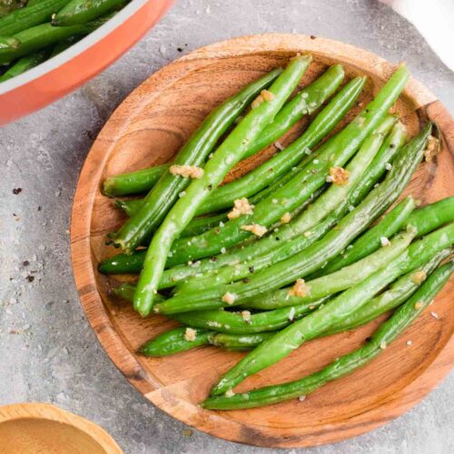 Steakhouse style garlic butter green beans on a wooden plate.