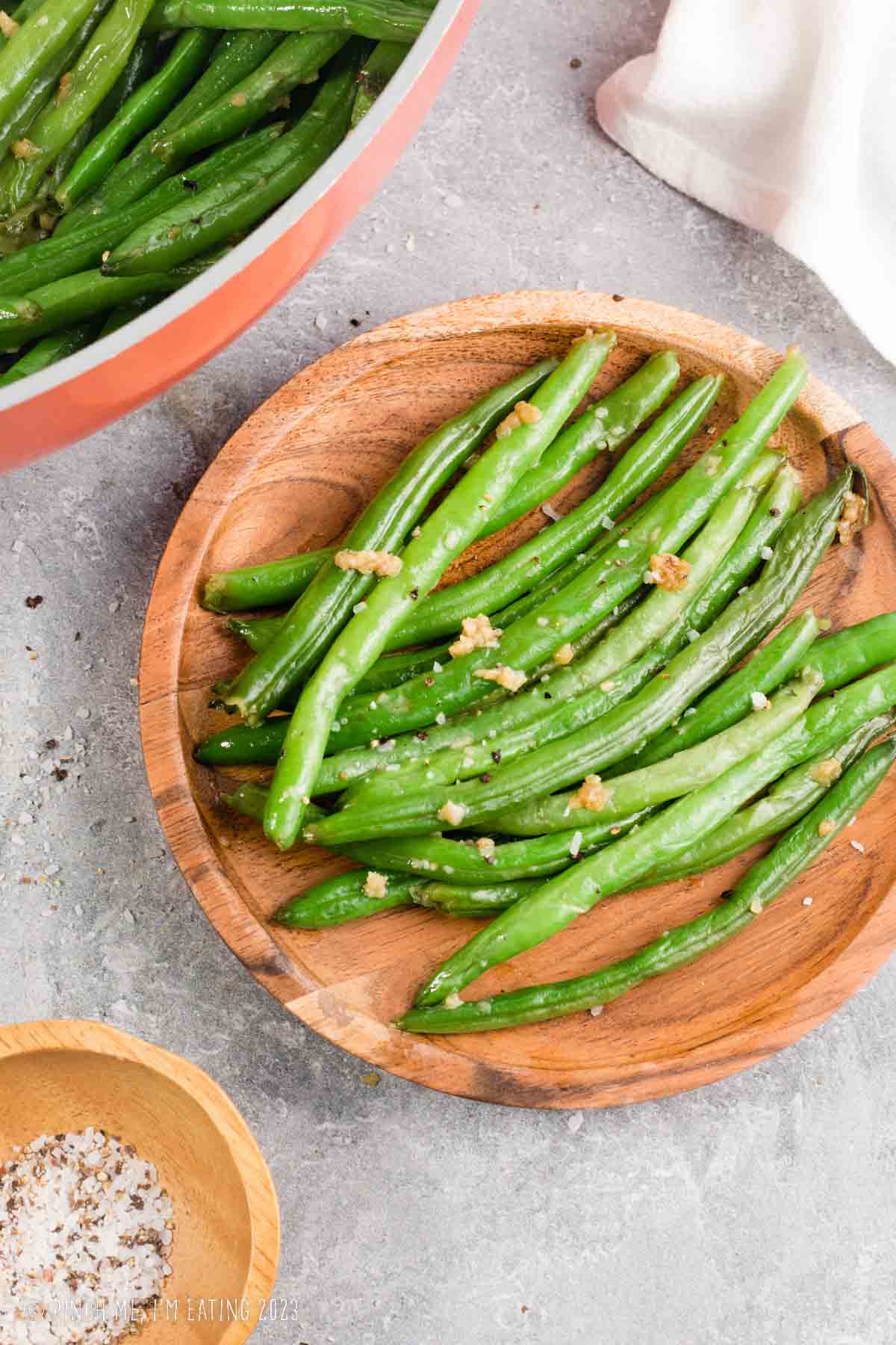 Steakhouse style garlic butter green beans on a wooden plate.