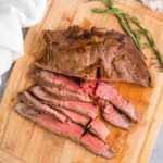 Medium rare flank steak marinated in red wine steak marinade sliced on a wooden cutting board with rosemary.