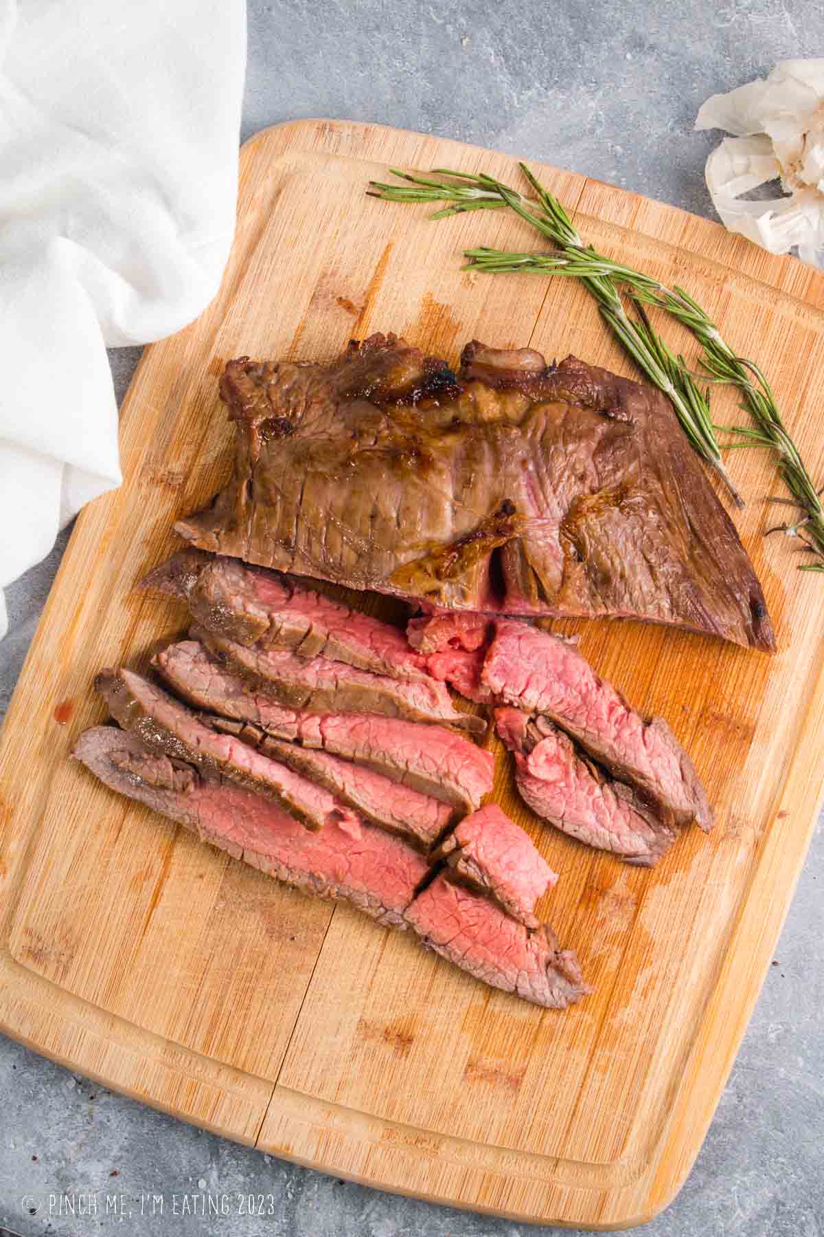 Medium rare flank steak marinated in red wine steak marinade sliced on a wooden cutting board with rosemary.