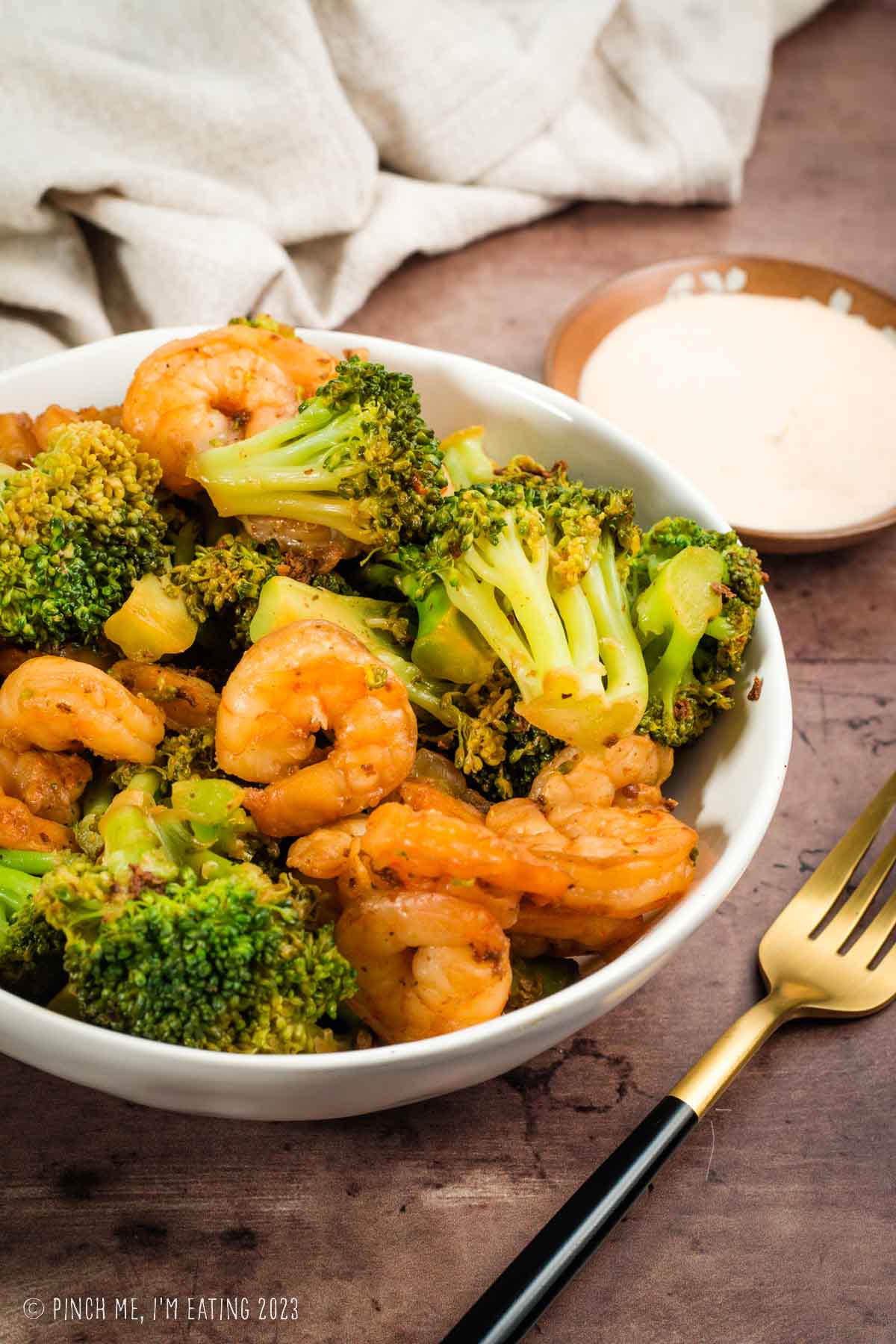 Hibachi shrimp and broccoli in white bowl with yum yum sauce on the side.