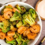Overhead view of hibachi shrimp and broccoli in white bowl with yum yum sauce on the side.