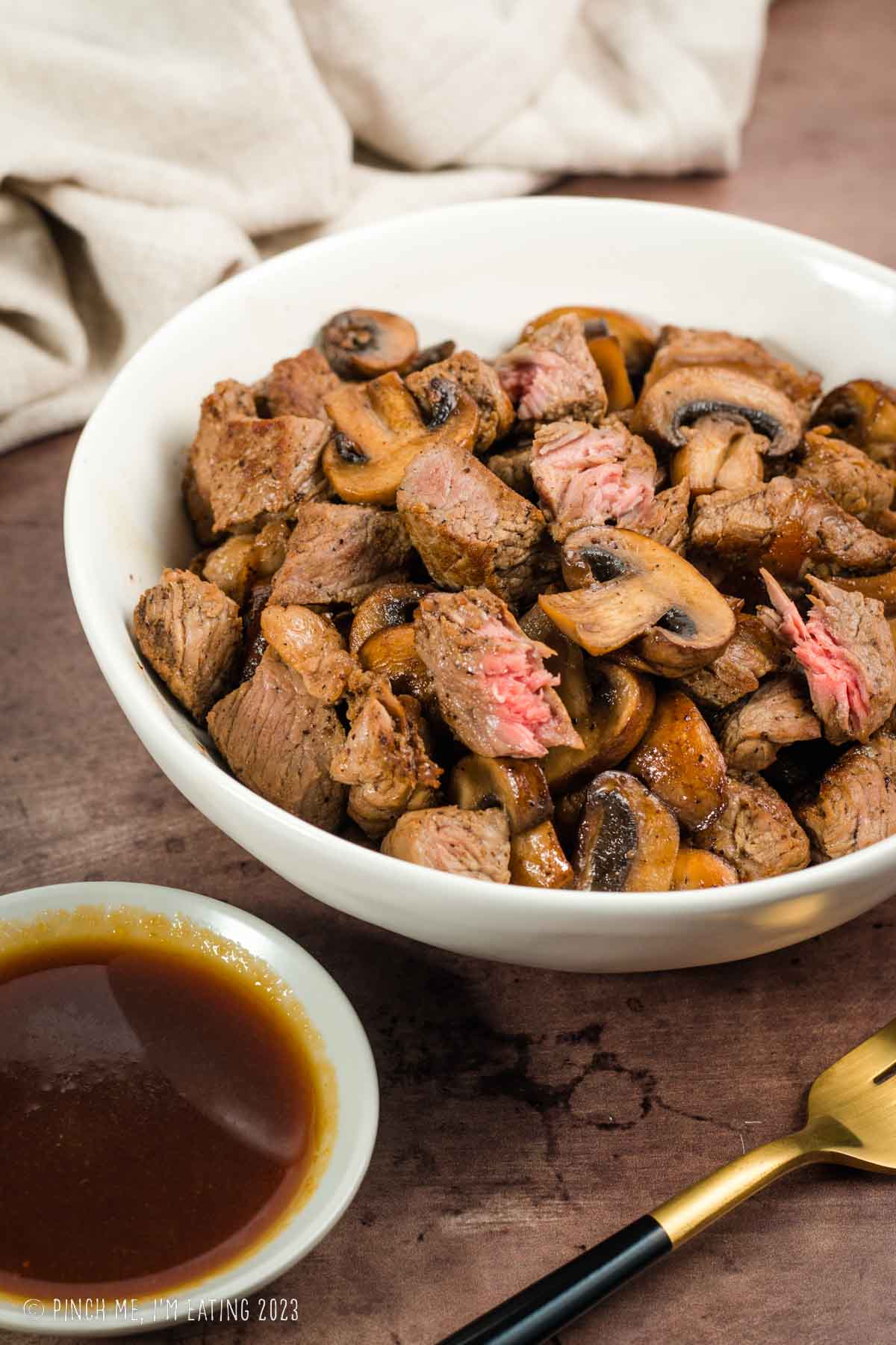 Hibachi steak and mushrooms in a white bowl with ginger dipping sauce.