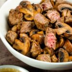 Hibachi steak and mushrooms in a white bowl with ginger dipping sauce.