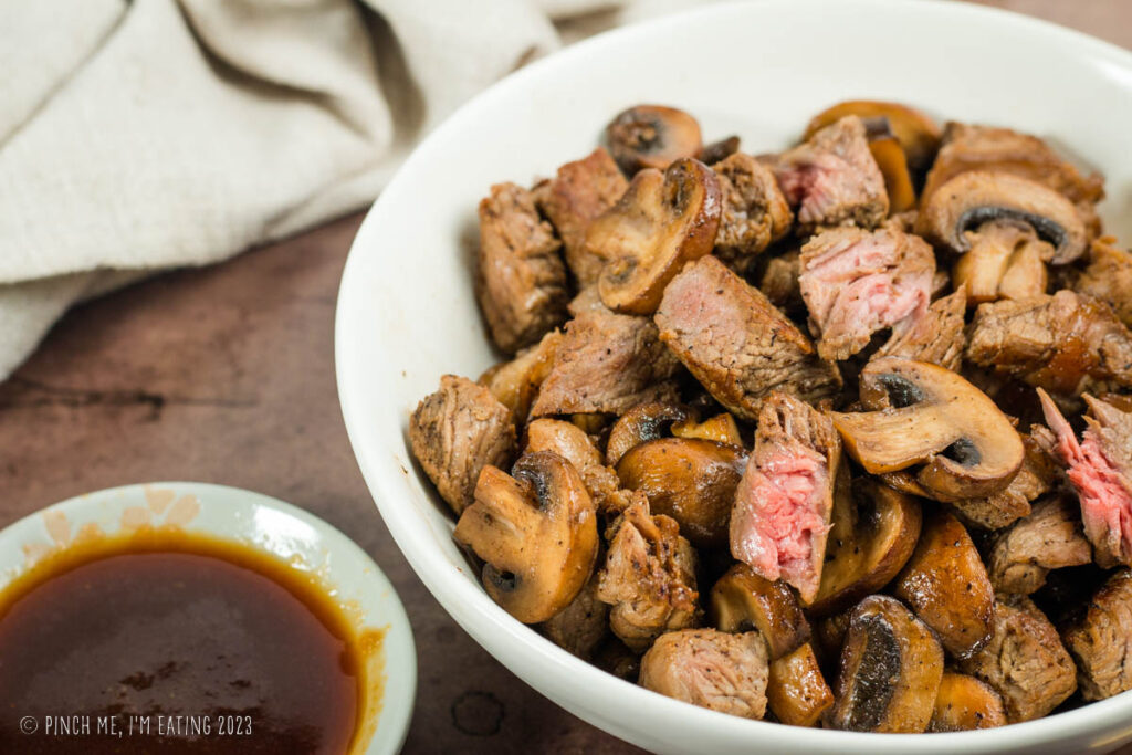 Hibachi steak and mushrooms in a white bowl with ginger dipping sauce.