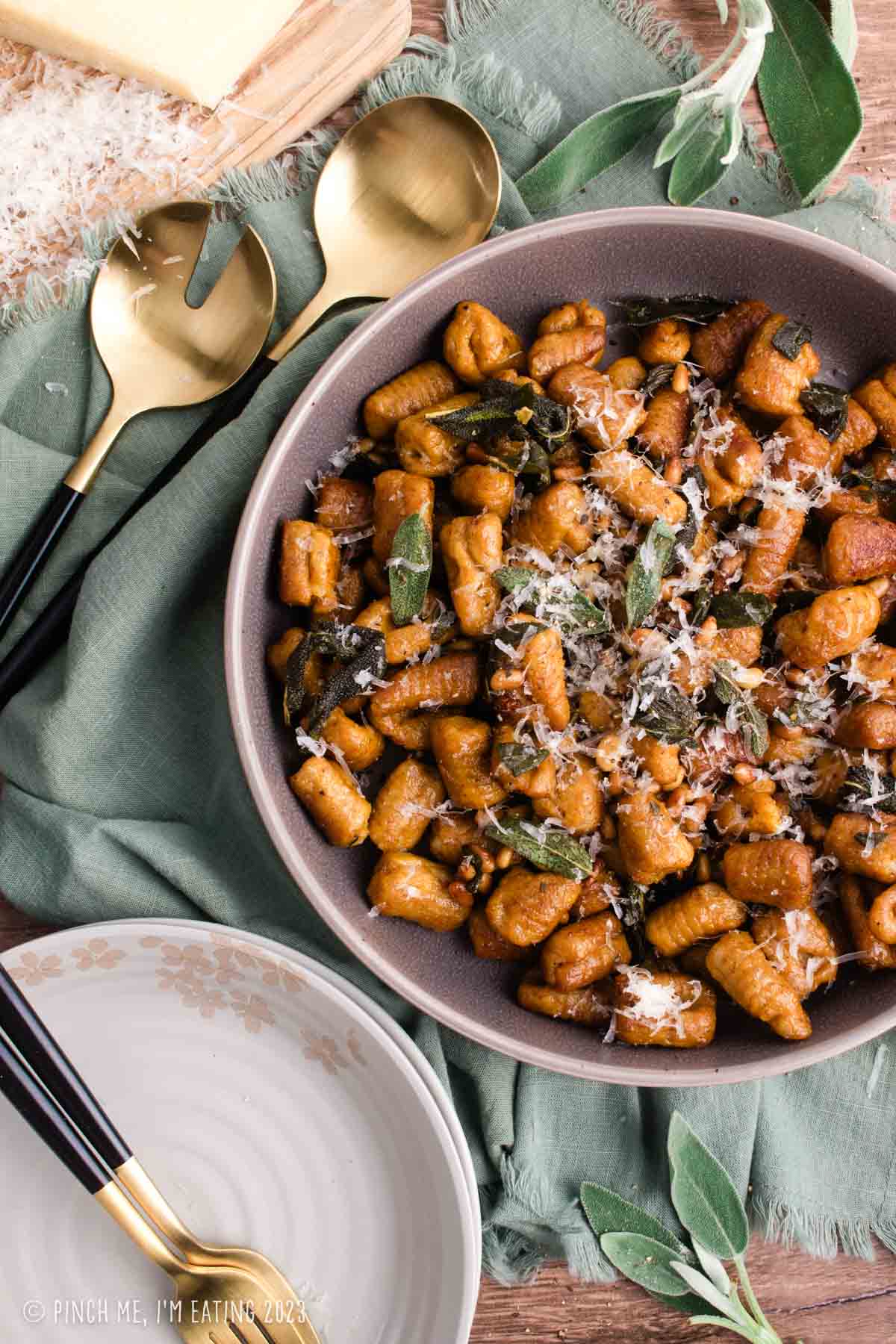 Homemade pumpkin gnocchi with crispy sage, pine nuts, and parmesan cheese in a gray serving bowl on a green napkin.