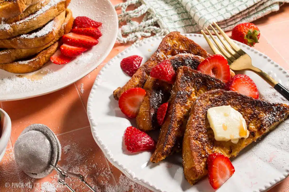 Sliced brioche French toast overlapping on a white plate with fresh strawberries.