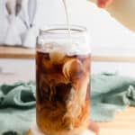Vanilla sweet cream pouring into cold brew coffee in a tall glass.