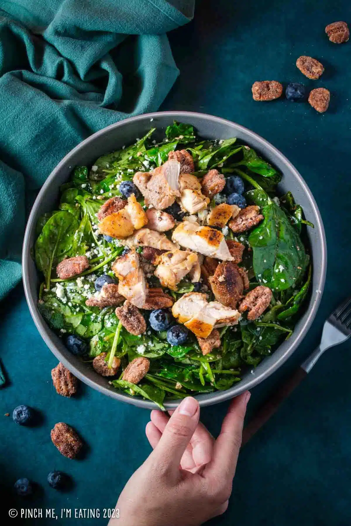 Spinach arugula salad with chicken, topped with blueberries, blue cheese, and pecans in a gray bowl.