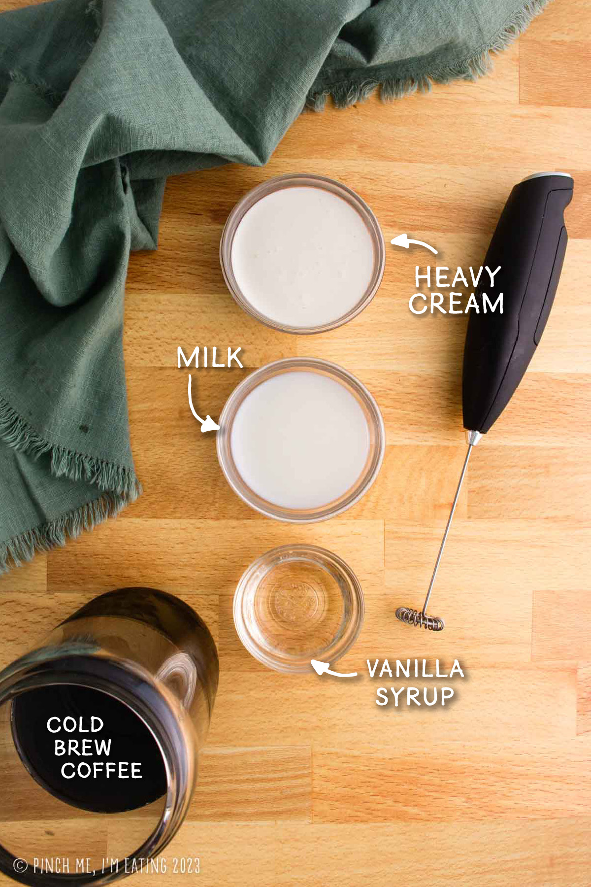 Ingredients for making sweet cream cold foam coffee, including an electric handheld milk frother and glass of cold brew coffee.