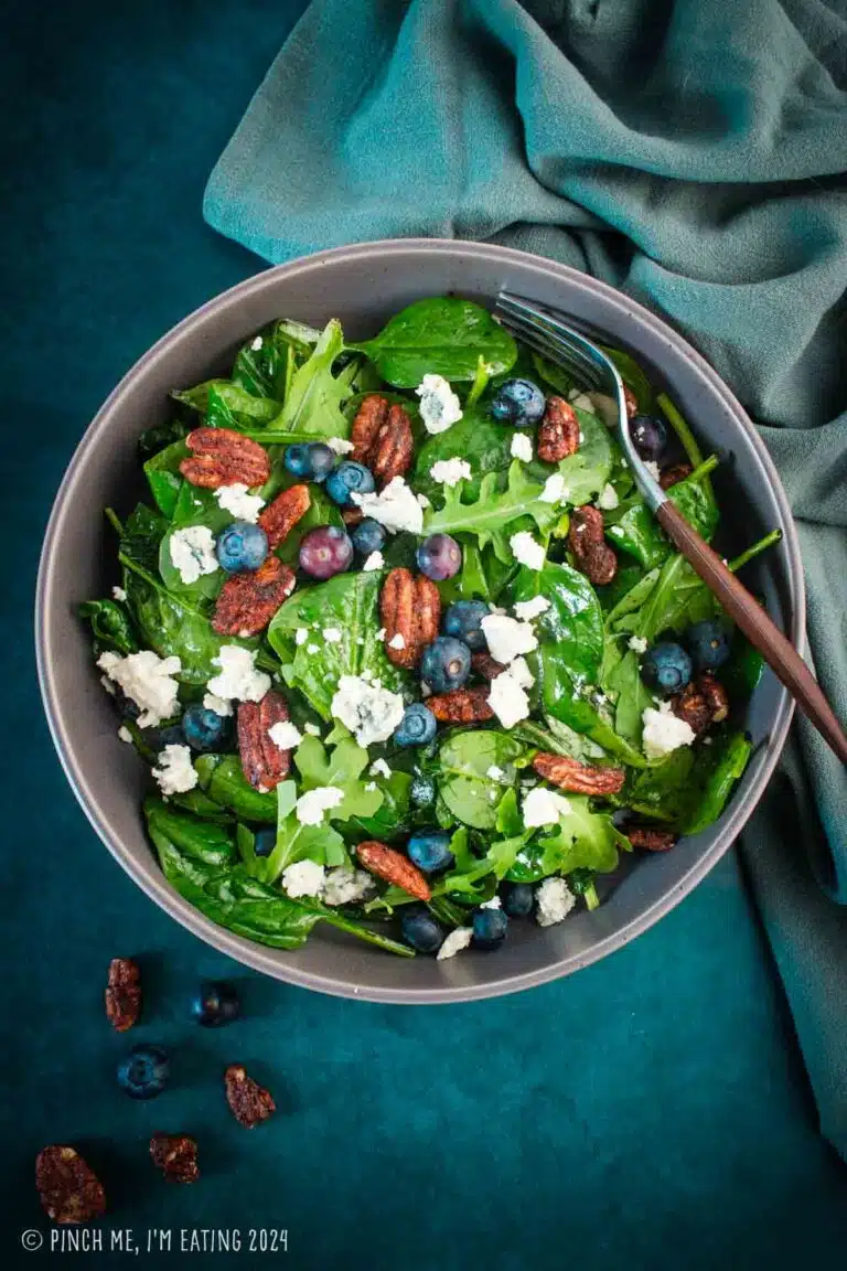 Spinach and arugula salad topped with blueberries, blue cheese, and pecans in a gray bowl.