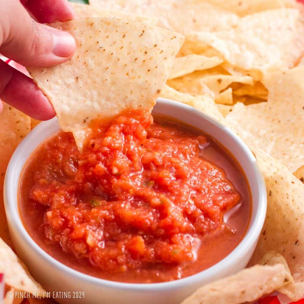 Restaurant-style blender salsa in a white bowl with a tortilla chip being dipped.
