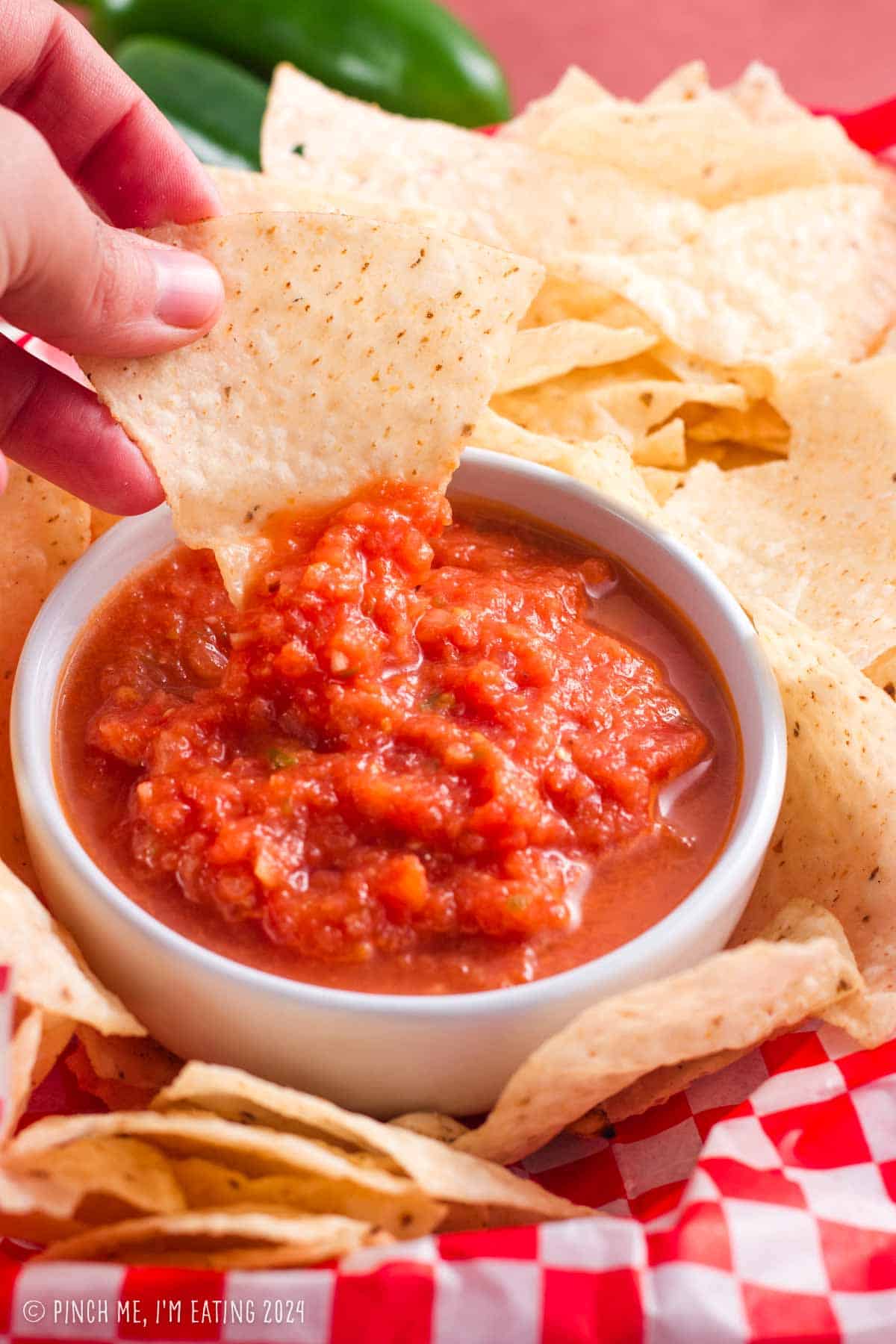 Restaurant-style blender salsa in a white bowl with a tortilla chip being dipped.